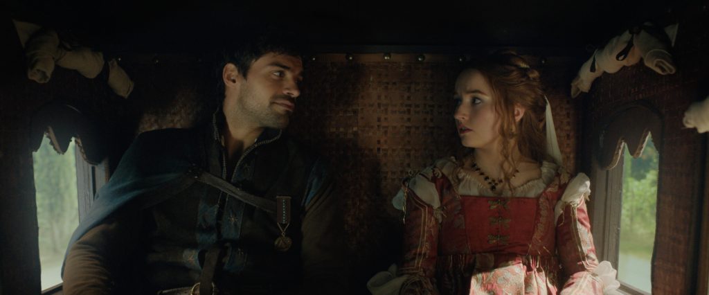 A production still from Rosaline. Lead characters Rosaline and Dario are sitting in a carriage, facing the camera but looking at each other.