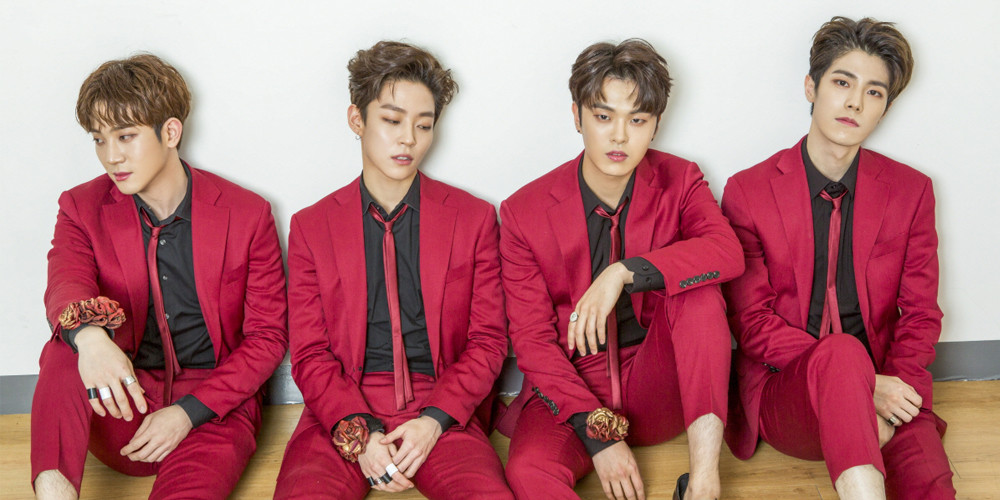 A promotional photo of The Rose. The four members are sitting in a line, all in pink suits, looking straight into the camera.