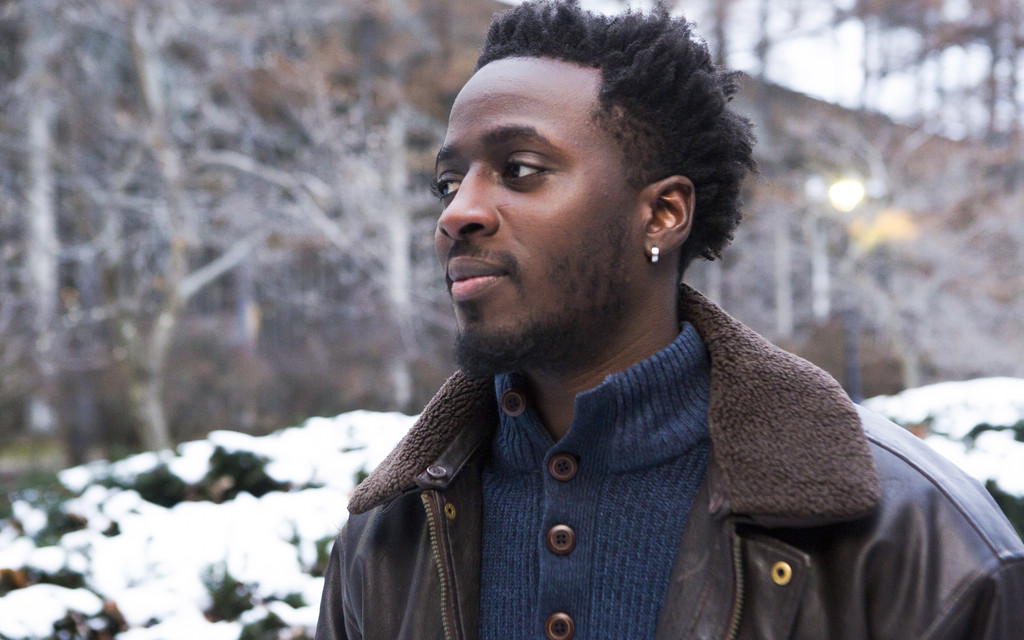 A profile photo of Nana Kwame Adjei-Brenyah. He is standing outside, with a snow covered landscape behind him, looking off to the left of the photo.