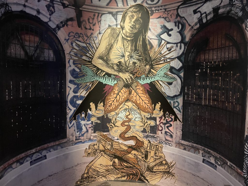A photo of a street art painting by Swoon. It shows a woman figure from nature rising out of a scene of industrial destruction.