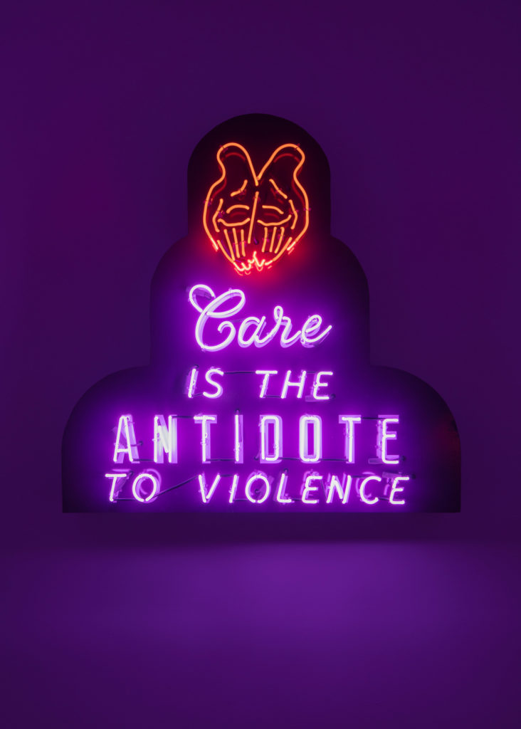 An image of an artwork by Ja'Tovia Gary. The piece consists of neon lighting in the shape of two palms and the words "Care is the Antidote to Violence" in purple writing.