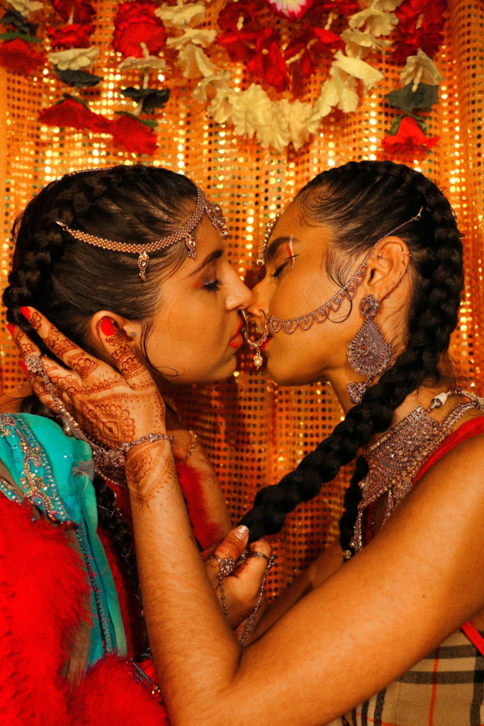 A photo of two Indian women, wearing traditional Indian clothing, holding each other and kissing in profile.