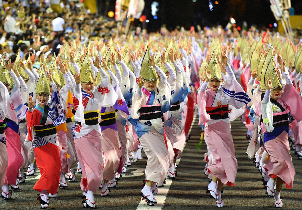A photo of a street filled with Awa Odori dancers. There are hundreds of them, all in lines, and the women are all standing on their front toes and holding their arms in the air.