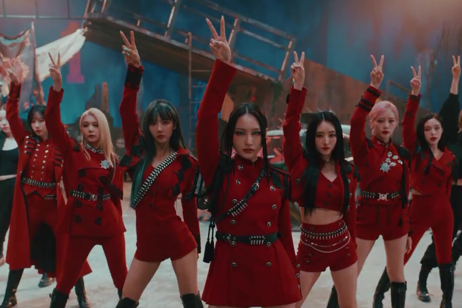 A photo still from the Vision video by Dreamcatcher. The members are mid-dance pose, one arm in the arm, all wearing red, staring directly into the camera.