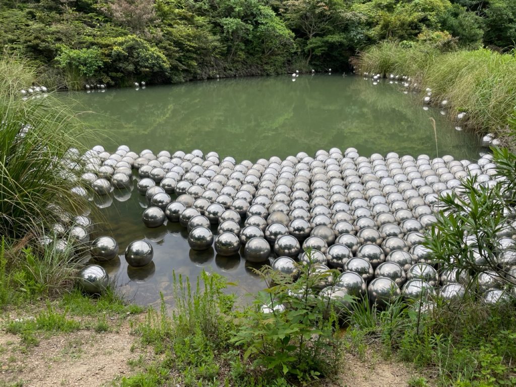 A photo of Narcissus Garden by Yayoi Kusama. It shows a pond with several dozen stainless steel spheres floating on the top of the water.