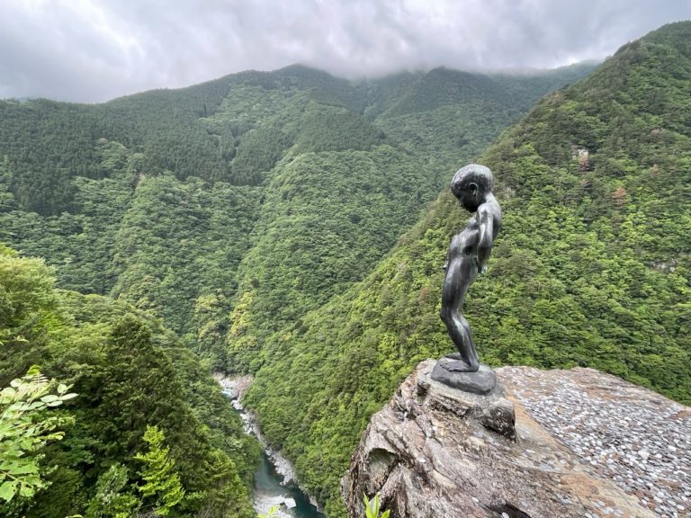 A photo of the Peeing Boy statue of Iya Valley. The photo shows the statue in the foreground and the gorge in the background.
