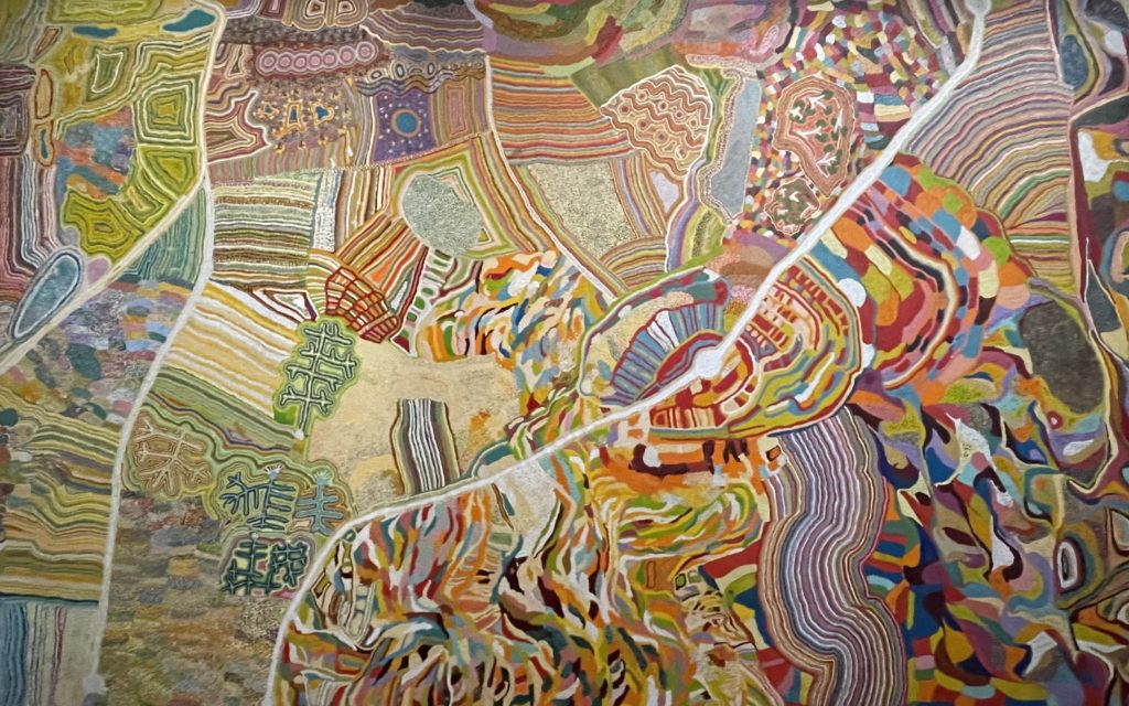 A image of a painting of one of the Seven Sisters songlines. It is a vibrantly coloured painting with one white path crossing down from the top right to the bottom left.