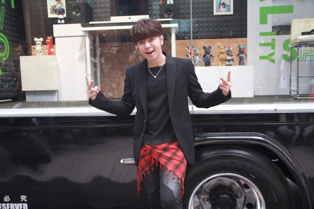 A photo of Show Lo, leaning against a vehicle, arms out to the side, posing directly into the camera.