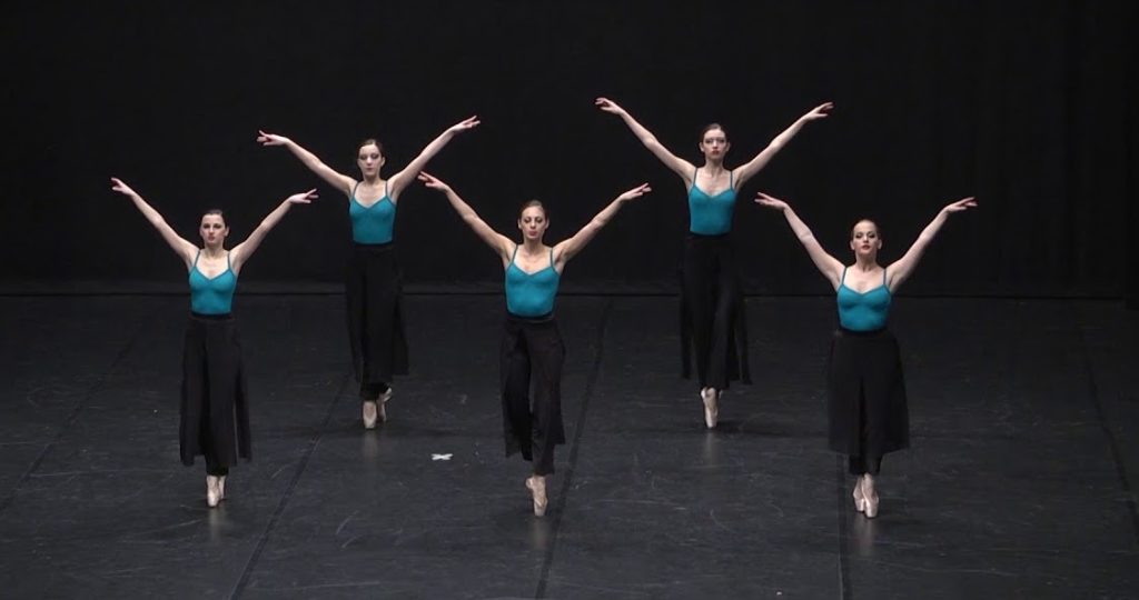 A photo still from a performance by Accademia Gaffurio di Lodi. Five dancers are standing onstage with their arms in the air in a V.
