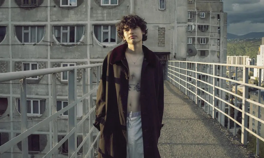A promotional photo of Glaive standing on a bridge looking straight into the camera.