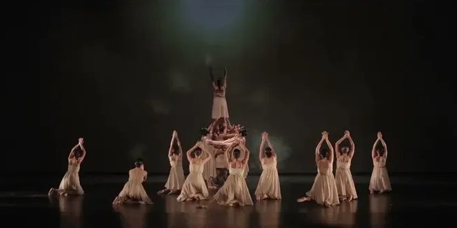 A photo still from Lenguaje by Mayra Ortega de León. A dozen dancers are seen onstage, most on their knees with their arms outstretched in the air.