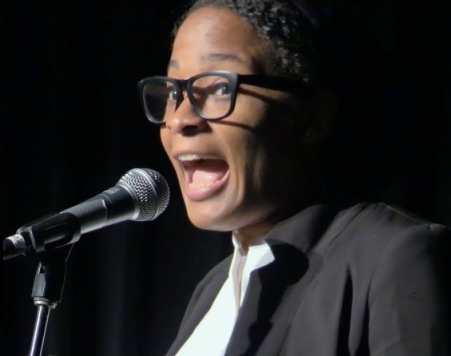 A close up photo of Jasmin Roberts speaking directly into a microphone onstage.