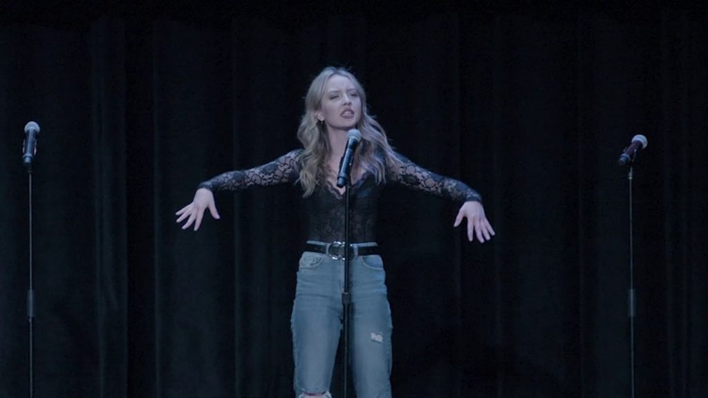 A photo of Maia Mayor onstage in front of a microphone, arms out to her sides, mid-performance.