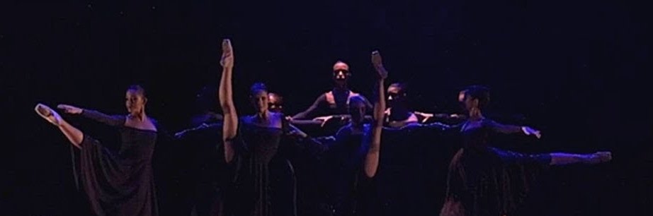 A photo still from Viribus Unites by Renata Araújo. Six dancers, all in black, are standing in a line, mid-performance onstage.
