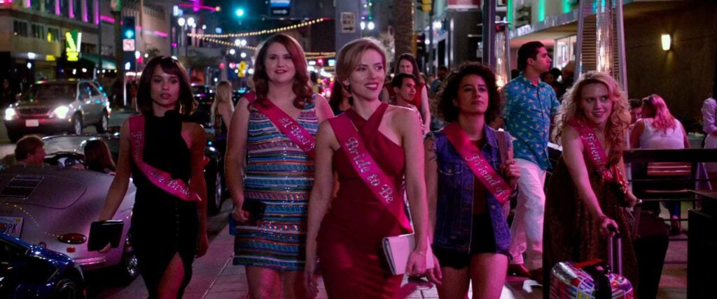 A photo still from Rough Night. It shows the five lead characters, all dressed up for a night out, walking down a street in a line in Miami.