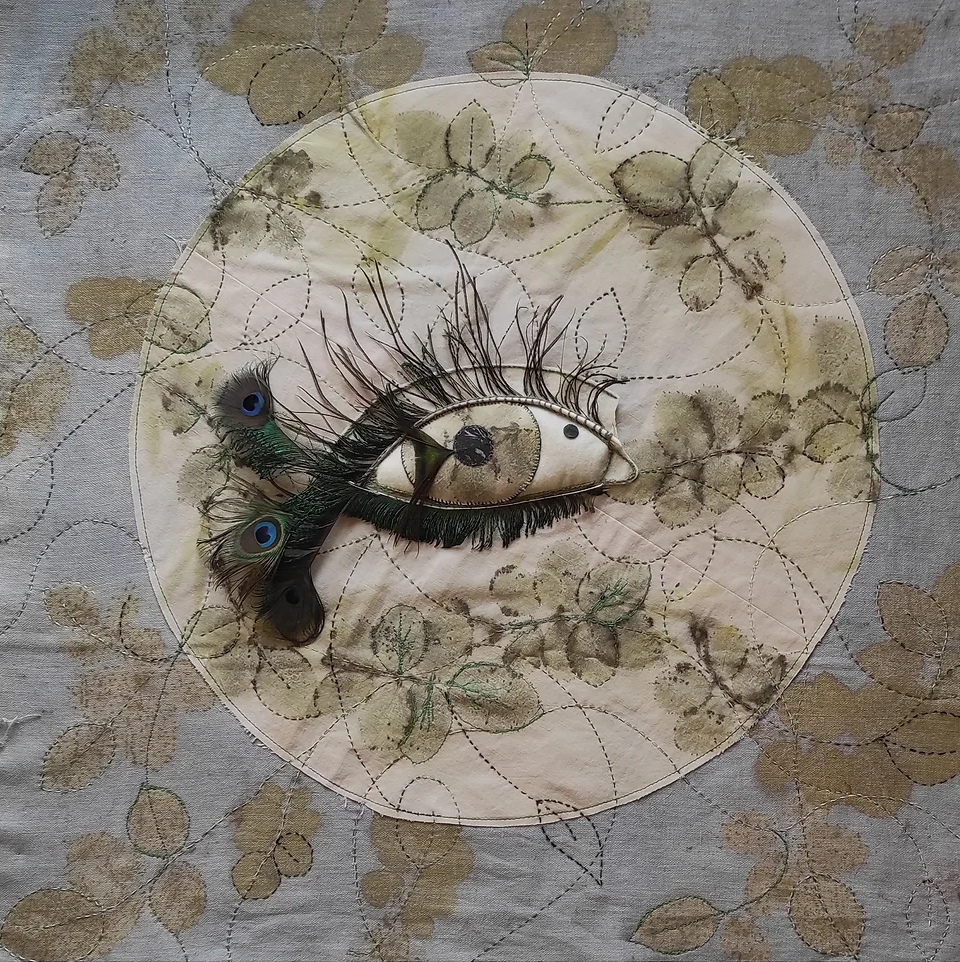 A vegetable art painting by Marie-Béatrice Jauzelon. It depicts a close up of an eye with long eyelashes, surrounded by green plants.